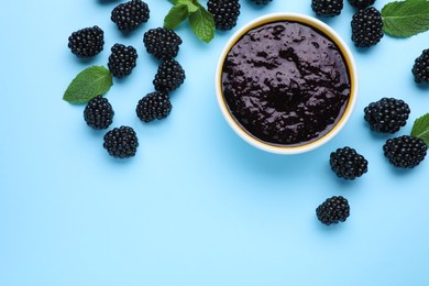 Photo of Blackberry puree in bowl and fresh berries on light blue background, flat lay. Space for text