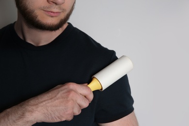 Man cleaning black t-shirt with lint roller on white background, closeup