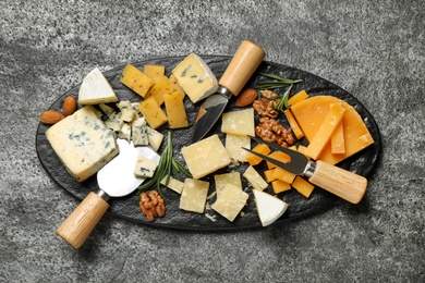 Photo of Cheese platter with specialized knives and fork on grey table, top view