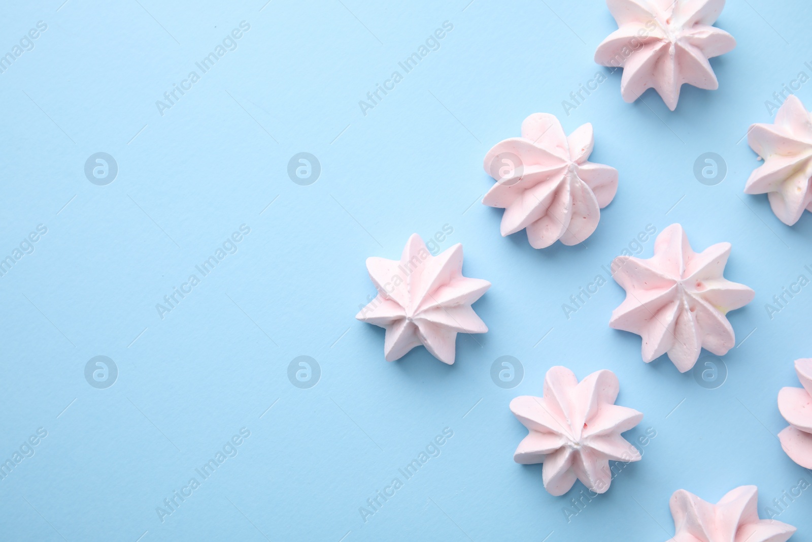 Photo of Tasty meringue cookies on light blue background, flat lay. Space for text