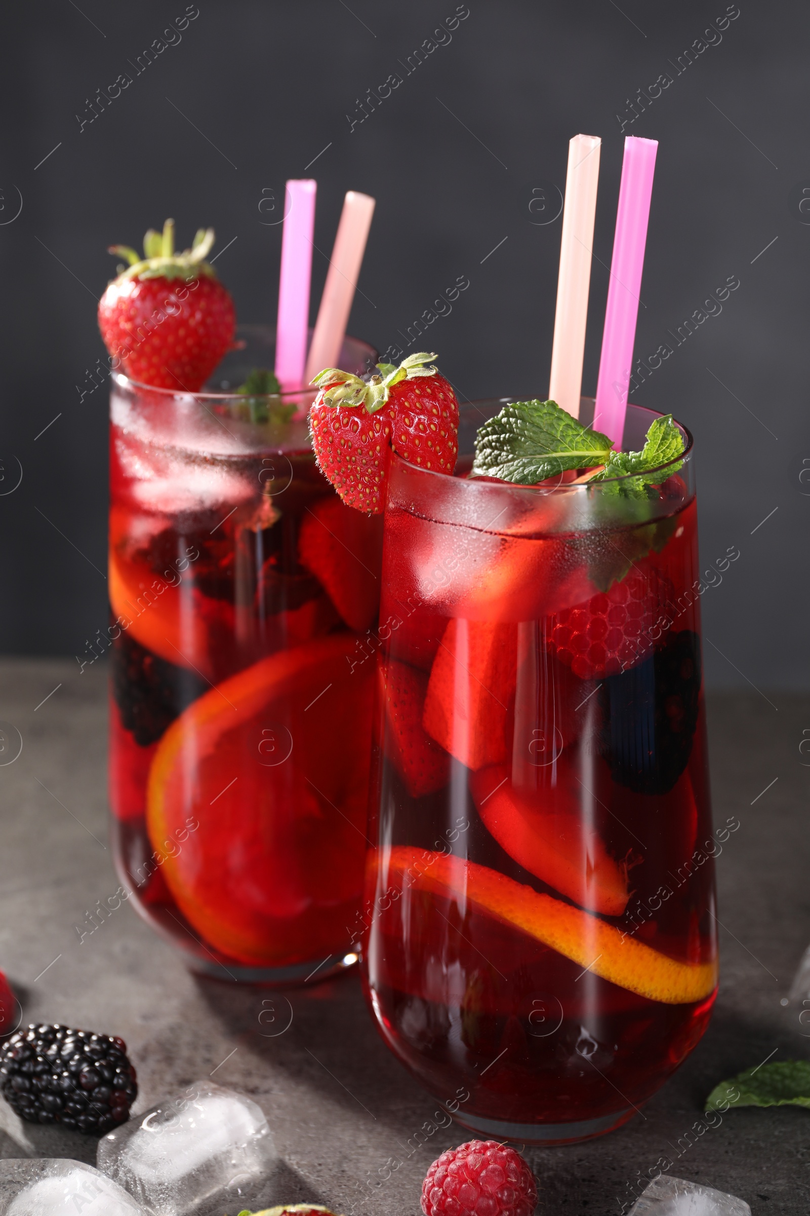 Photo of Glasses of delicious refreshing sangria, ice cubes and berries on grey table