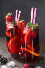 Glasses of delicious refreshing sangria, ice cubes and berries on grey table