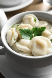 Photo of Bowl of tasty dumplings in broth on table, closeup