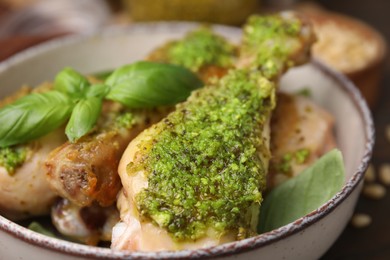 Photo of Delicious fried chicken drumsticks with pesto sauce and basil in bowl, closeup