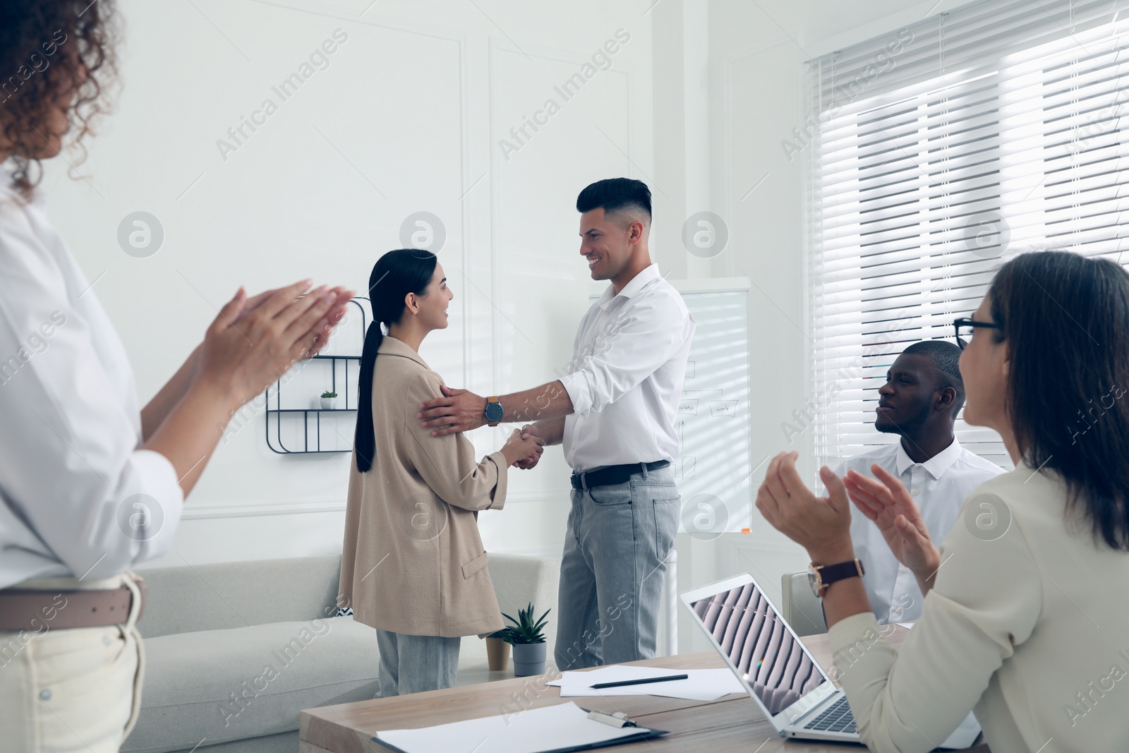 Photo of Boss shaking hand with new employee and coworkers applauding in office