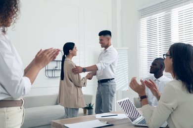 Boss shaking hand with new employee and coworkers applauding in office