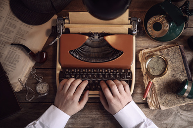 Detective working on vintage typewriter at wooden table, top view