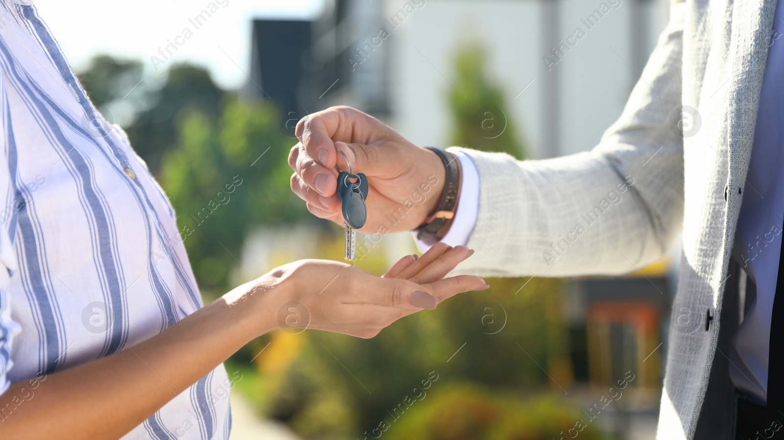 Photo of Real estate agent giving house keys to young woman outdoors, closeup