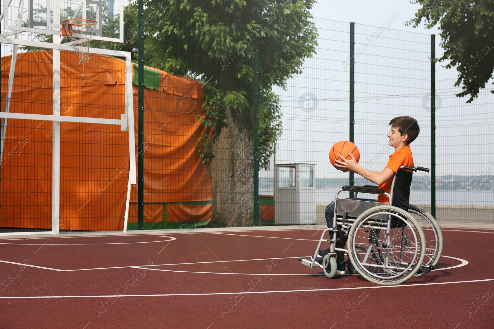 Photo of Disabled teenage boy in wheelchair playing basketball  on outdoor court