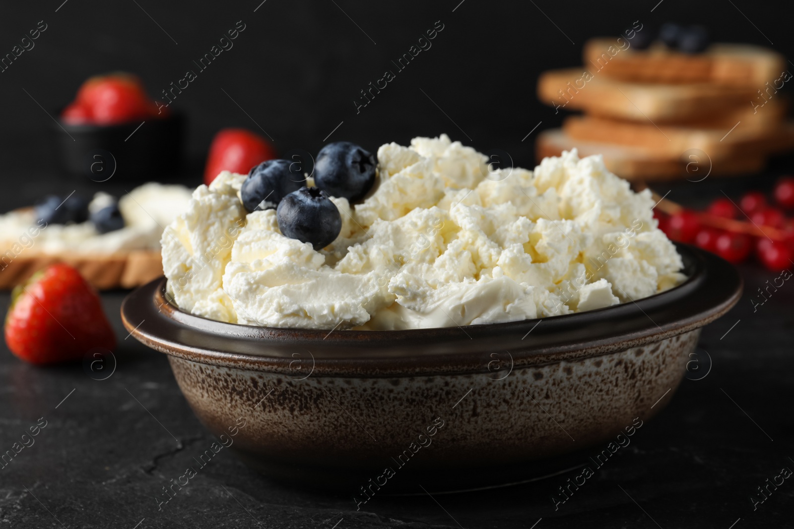 Photo of Tasty cream cheese and fresh berries on black table
