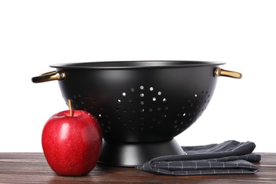 Black colander, apple and napkin on wooden table against white background