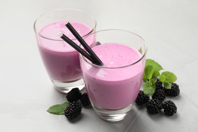 Photo of Delicious blackberry smoothie in glasses, fresh berries and mint on grey table