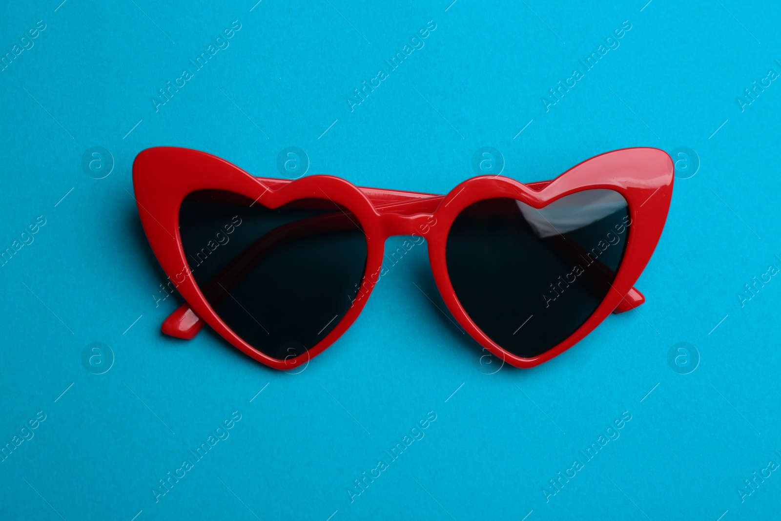 Photo of Stylish heart shaped sunglasses on blue background, top view. Fashionable accessory