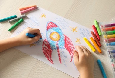 Photo of Little boy drawing rocket with soft pastel at wooden table, above view. Child`s art