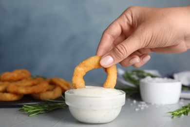 Photo of Woman dipping crunchy fried onion ring in sauce, closeup