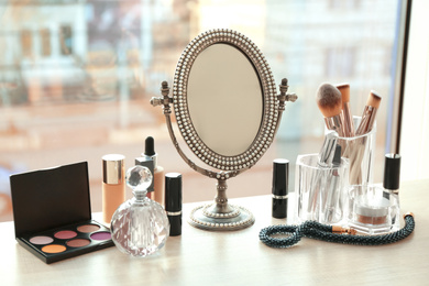 Photo of Mirror and makeup products on table near window indoors