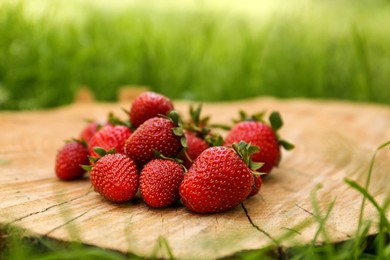 Photo of Pile of delicious ripe strawberries on tree stump outdoors, closeup