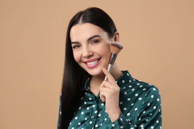 Photo of Happy woman with makeup brush on light brown background