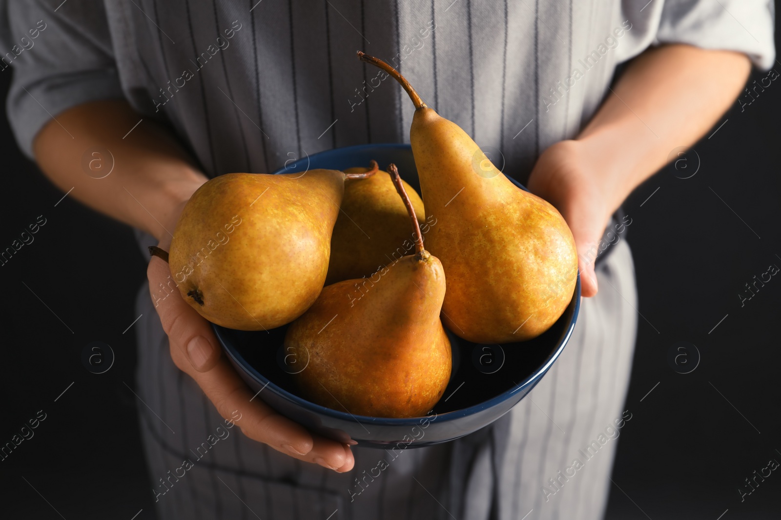 Photo of Woman holding bowl with ripe pears on black background, closeup