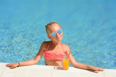 Photo of Cute little girl with glass of juice at swimming pool edge on sunny day
