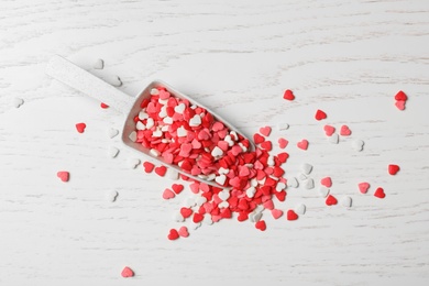 Photo of Bright heart shaped sprinkles and scoop on white wooden table, flat lay