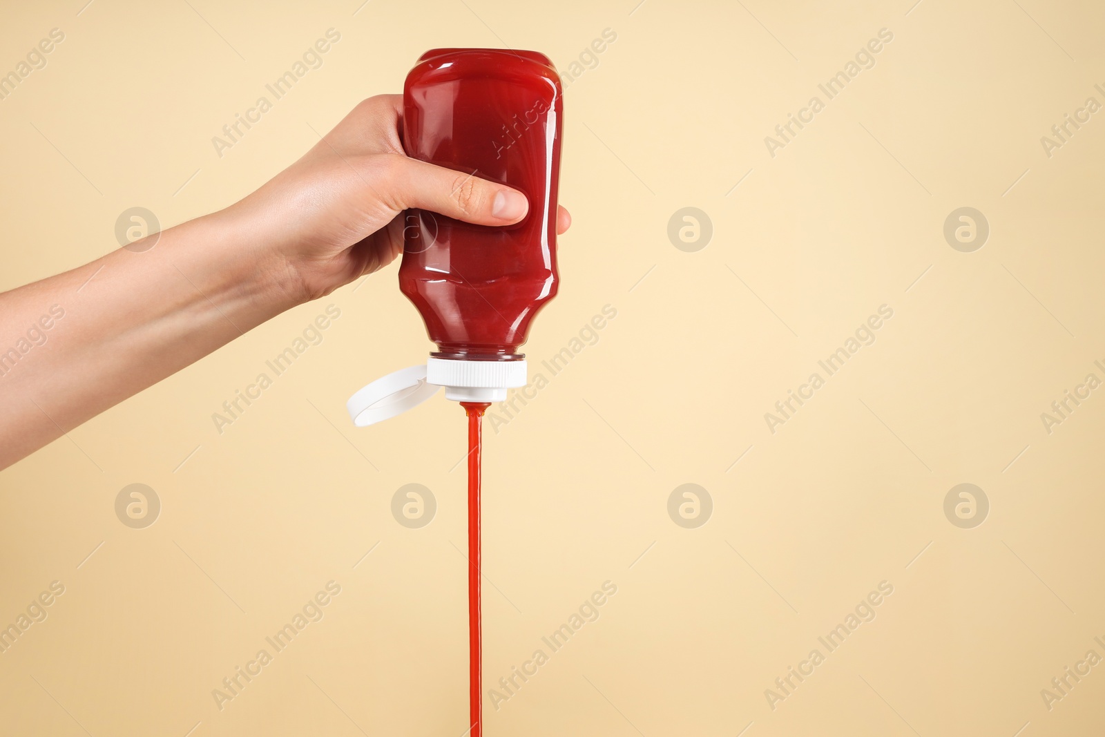 Photo of Woman pouring tasty ketchup from bottle on beige background, closeup. Space for text