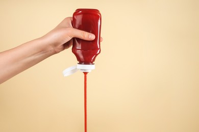 Woman pouring tasty ketchup from bottle on beige background, closeup. Space for text