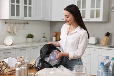 Smiling woman separating garbage in kitchen. Space for text