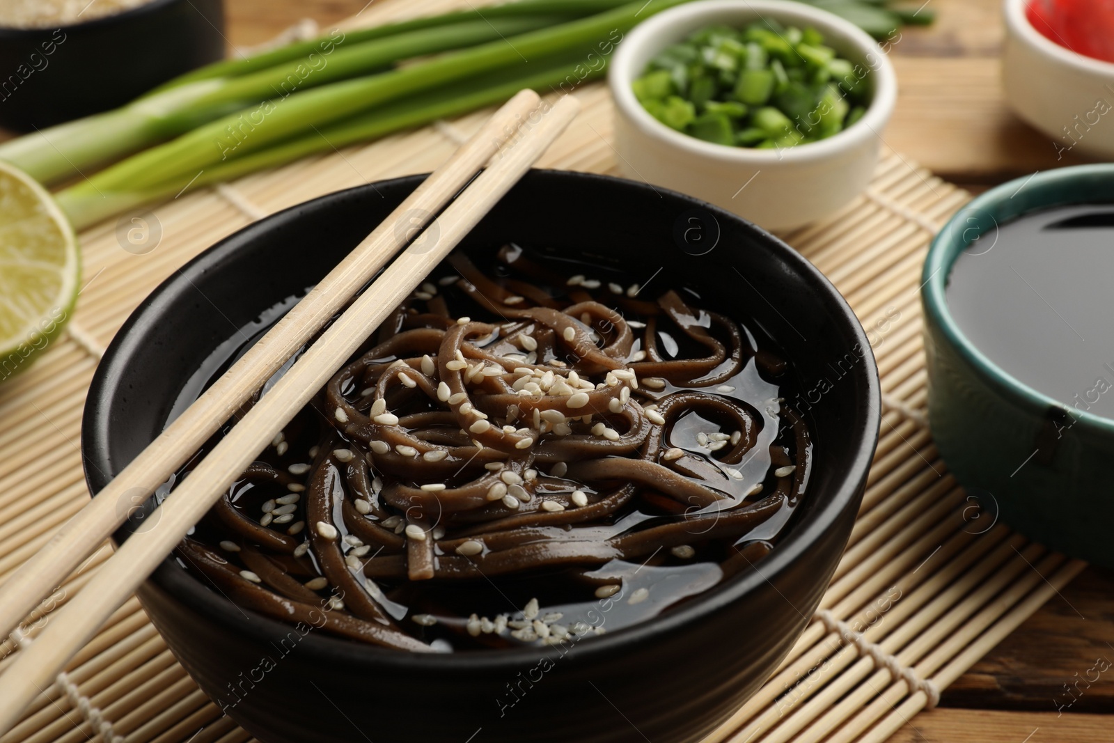 Photo of Tasty soup with buckwheat noodles (soba), sesame and chopsticks on table