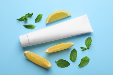 Photo of Blank tube of toothpaste with mint leaves and lemon slices on turquoise background, flat lay