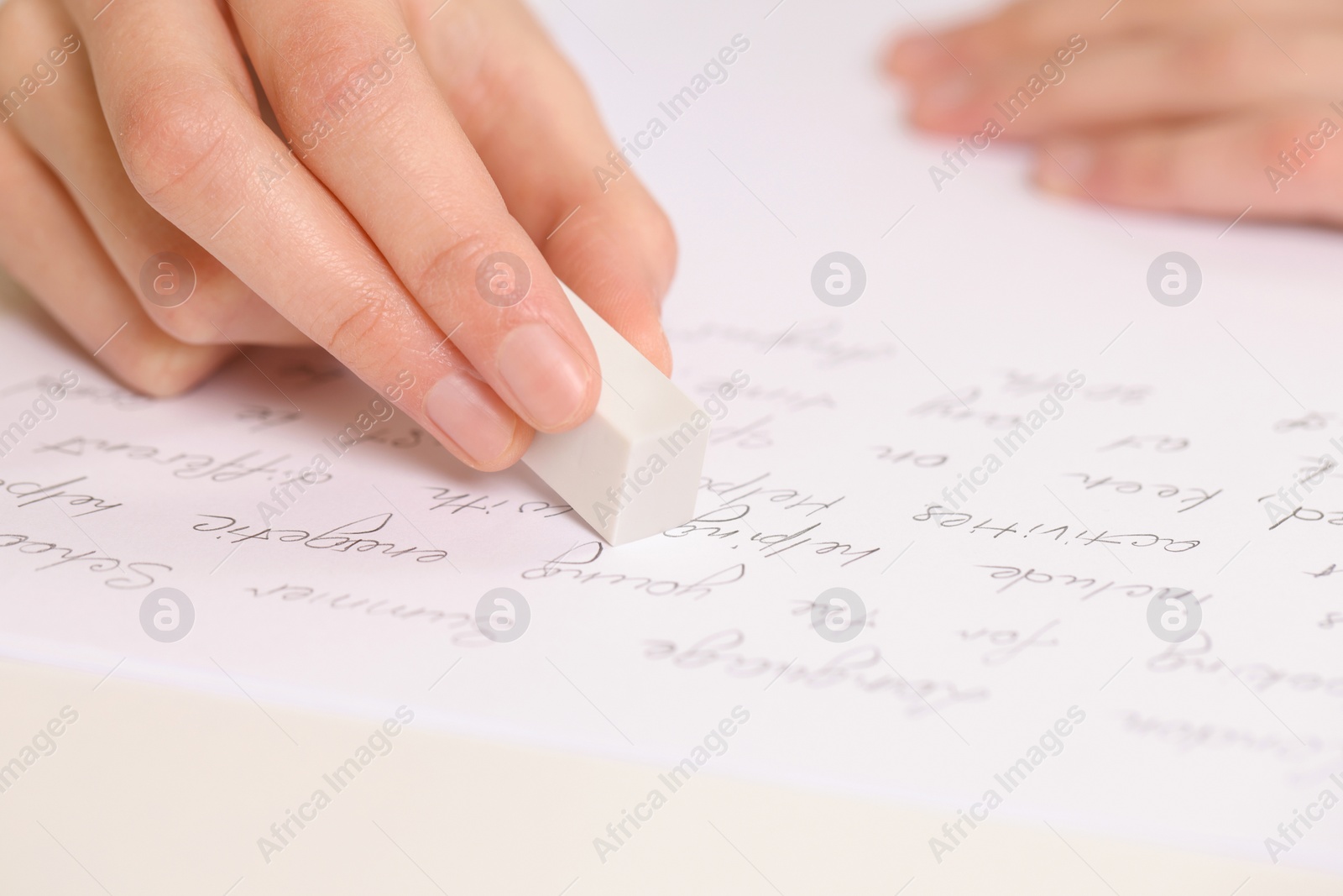 Photo of Boy erasing mistake in his notebook at white desk, closeup