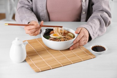 Photo of Woman eating delicious ramen with chopsticks at white table, closeup. Noodle soup