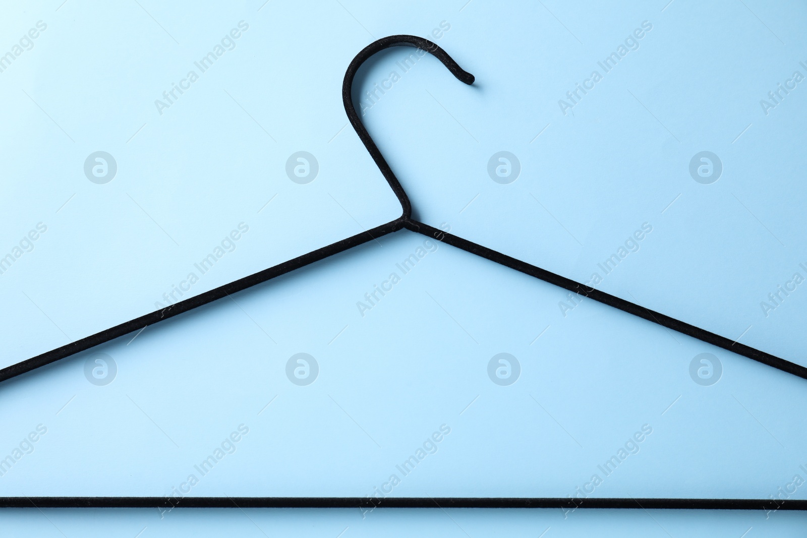 Photo of One black hanger on light blue background, top view