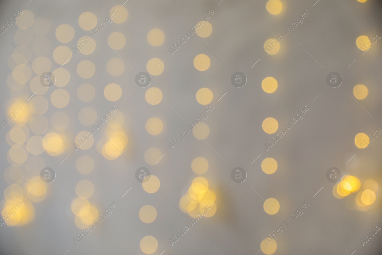 Photo of Blurred view of Christmas fairy lights on grey wall. Interior decoration