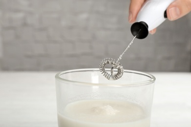 Photo of Woman using milk frother on blurred background, closeup