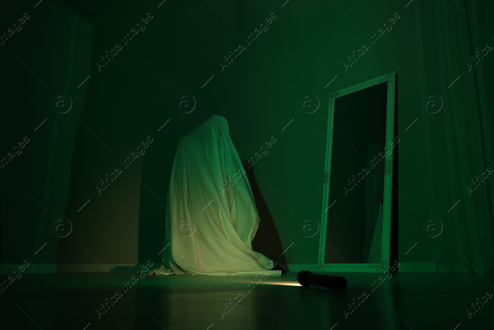 Photo of Creepy ghost. Woman covered with sheet near mirror in green light