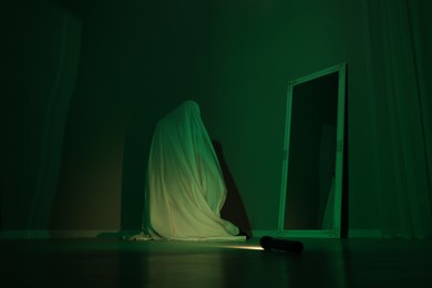 Creepy ghost. Woman covered with sheet near mirror in green light