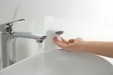 Photo of Woman using automatic soap dispenser in bathroom, closeup