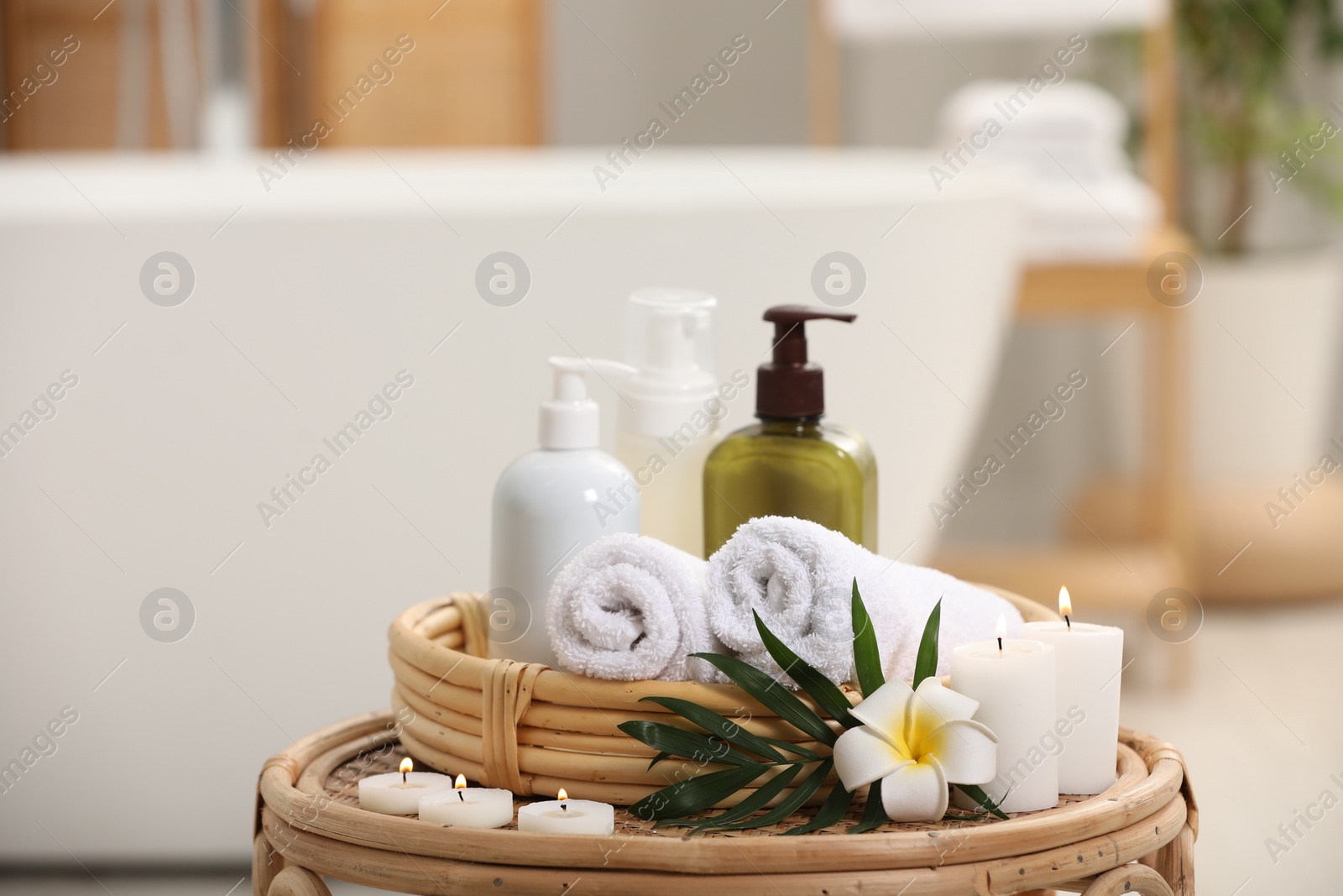 Photo of Spa products, burning candles, plumeria flower and tropical leaf on table in bathroom. Space for text