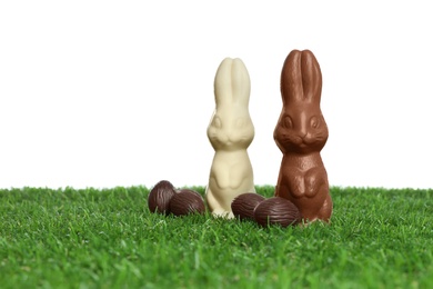 Photo of Chocolate bunnies and eggs on green grass against white background, space for text. Easter celebration