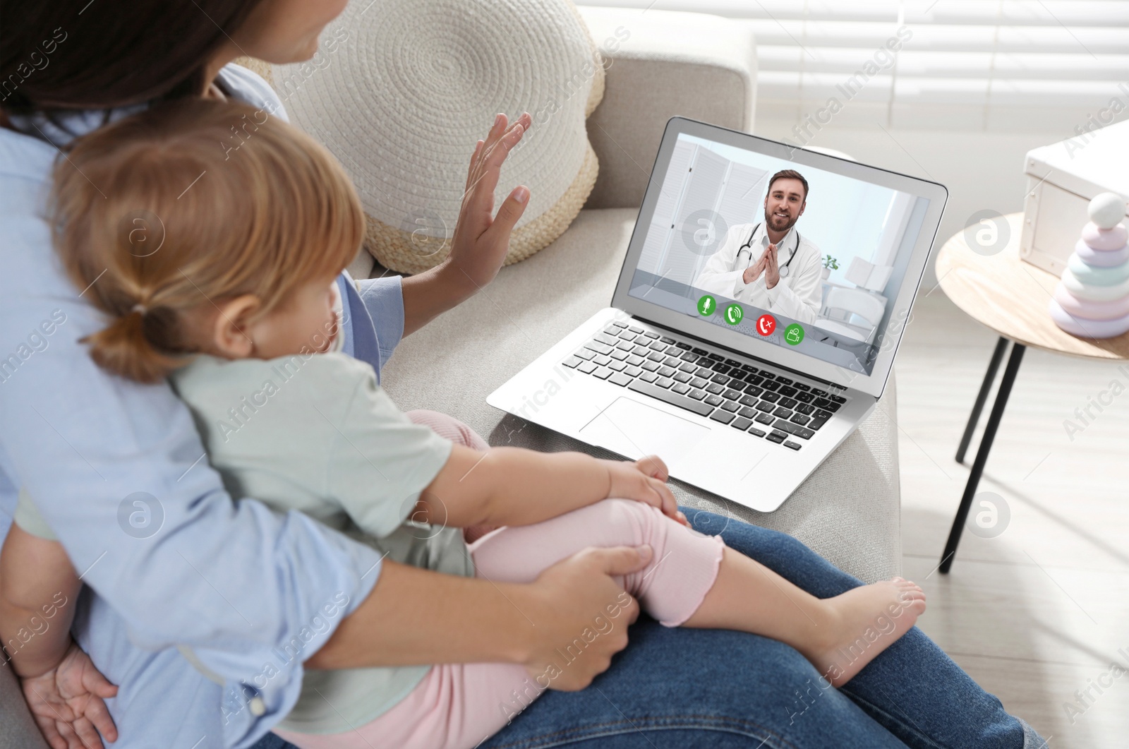 Image of Mother and daughter having online consultation with pediatrician via laptop on sofa at home