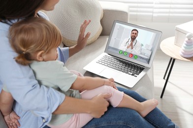 Mother and daughter having online consultation with pediatrician via laptop on sofa at home