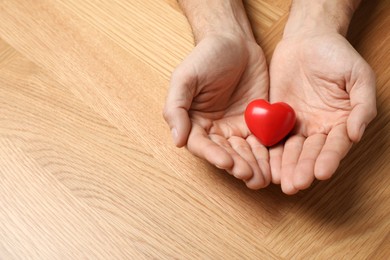 Photo of Man holding red heart in hands at wooden table, closeup. Space for text