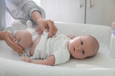 Mother putting clothes on her little baby at changing table indoors, closeup