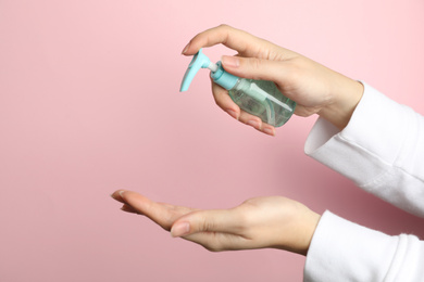Photo of Woman applying antiseptic gel on hand against pink background, closeup