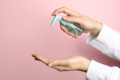 Woman applying antiseptic gel on hand against pink background, closeup