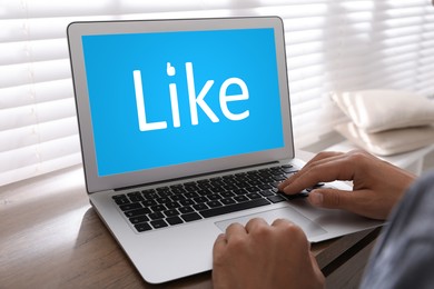 Image of Man using laptop with word Like on screen at wooden table, closeup