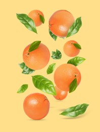 Image of Tasty ripe grapefruits and green leaves falling on beige background