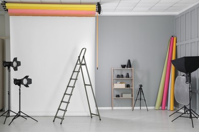 Photo of White photo background, ladder and professional lighting equipment in modern studio