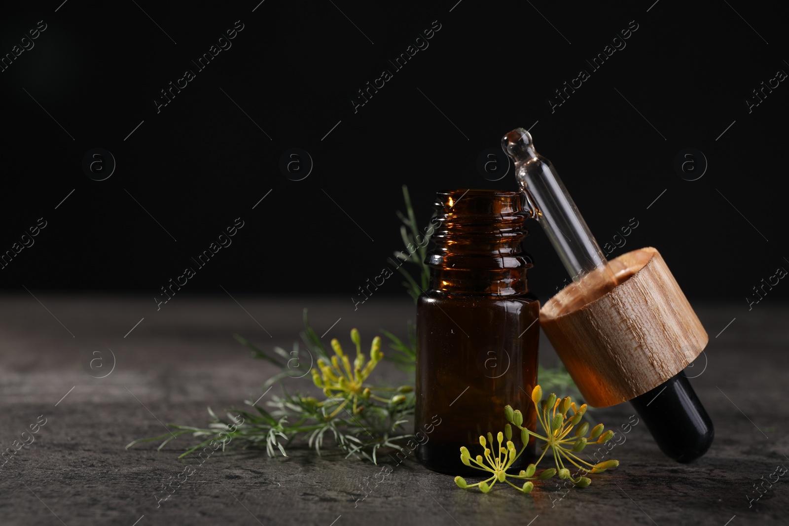 Photo of Bottle of essential oil, pipette and fresh dill on grey table, closeup. Space for text